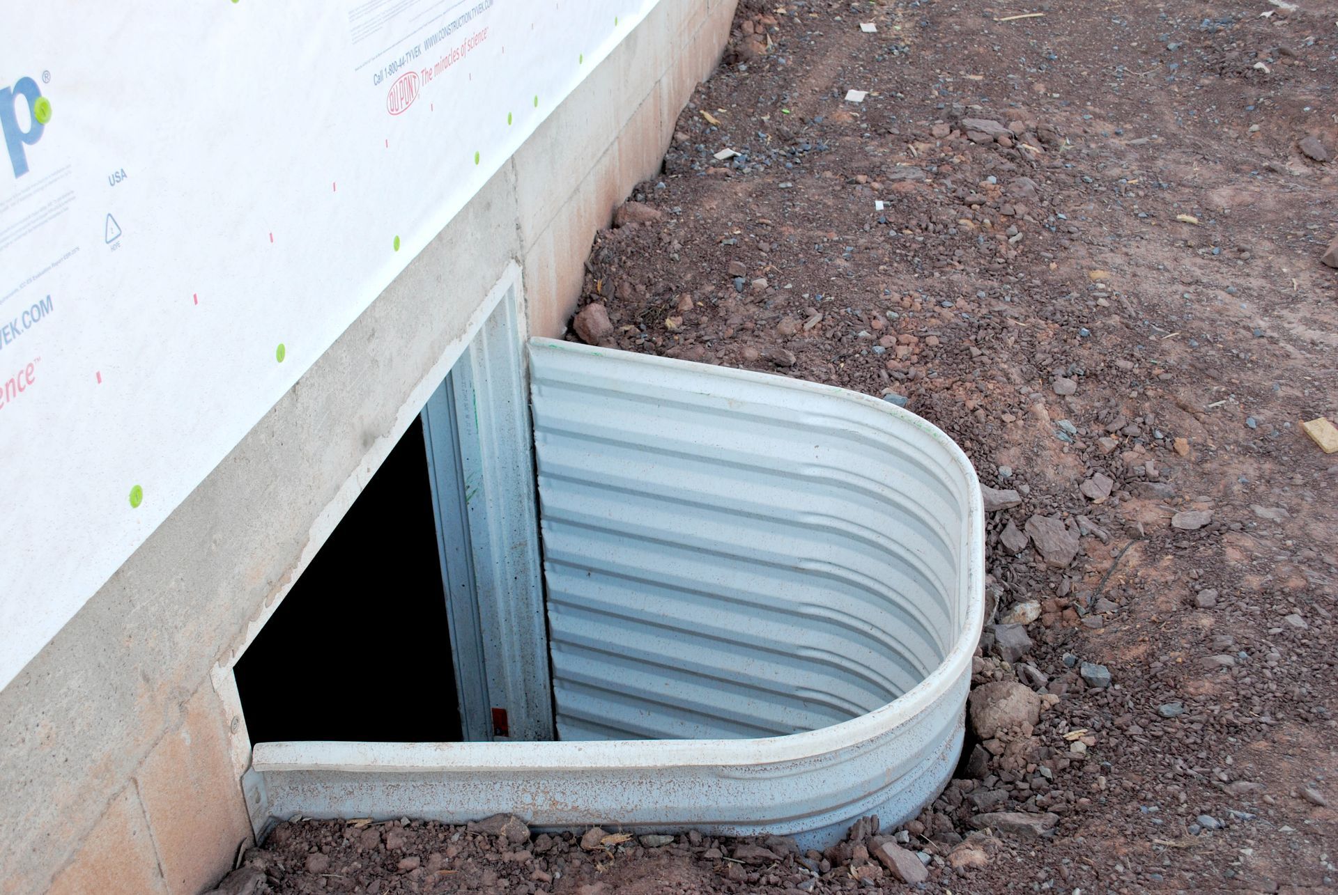 Basement window well with corrugated metal cover beside a house foundation