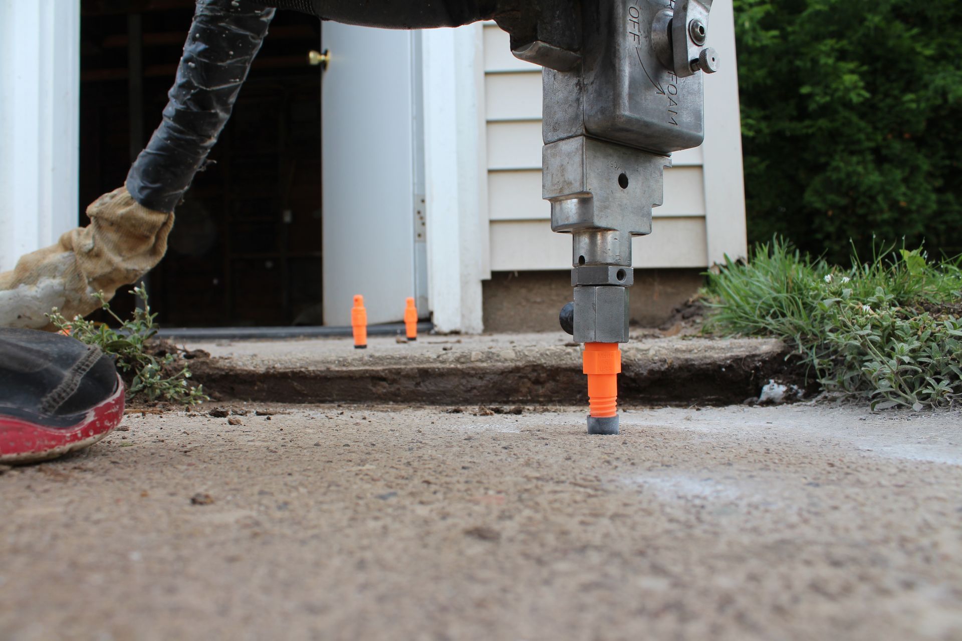 A close-up of a jackhammer tool drilling into a concrete sidewalk in front of a building.