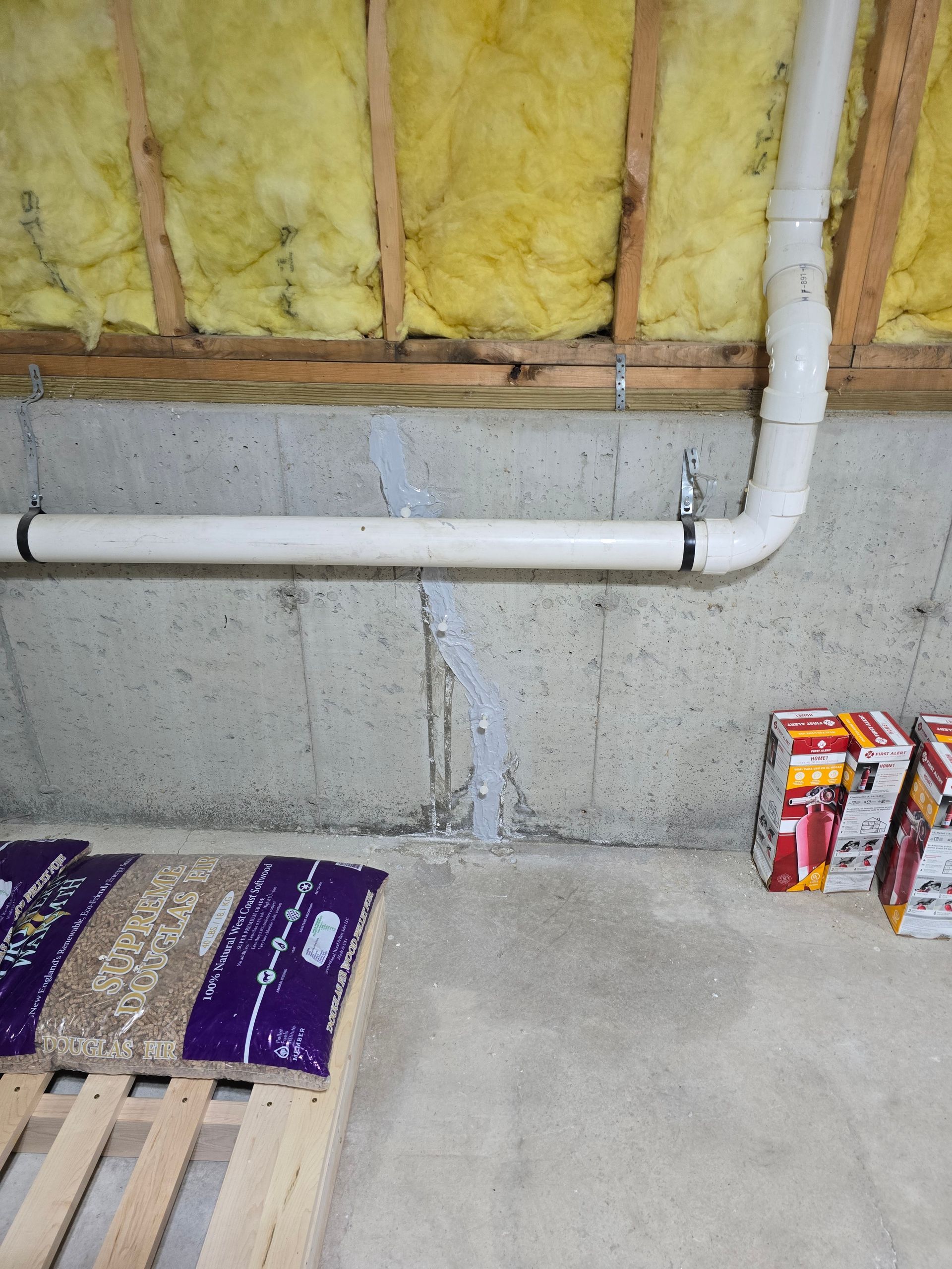 A vertical crack in a basement concrete wall has been patched with sealant, with white PVC piping running horizontally.