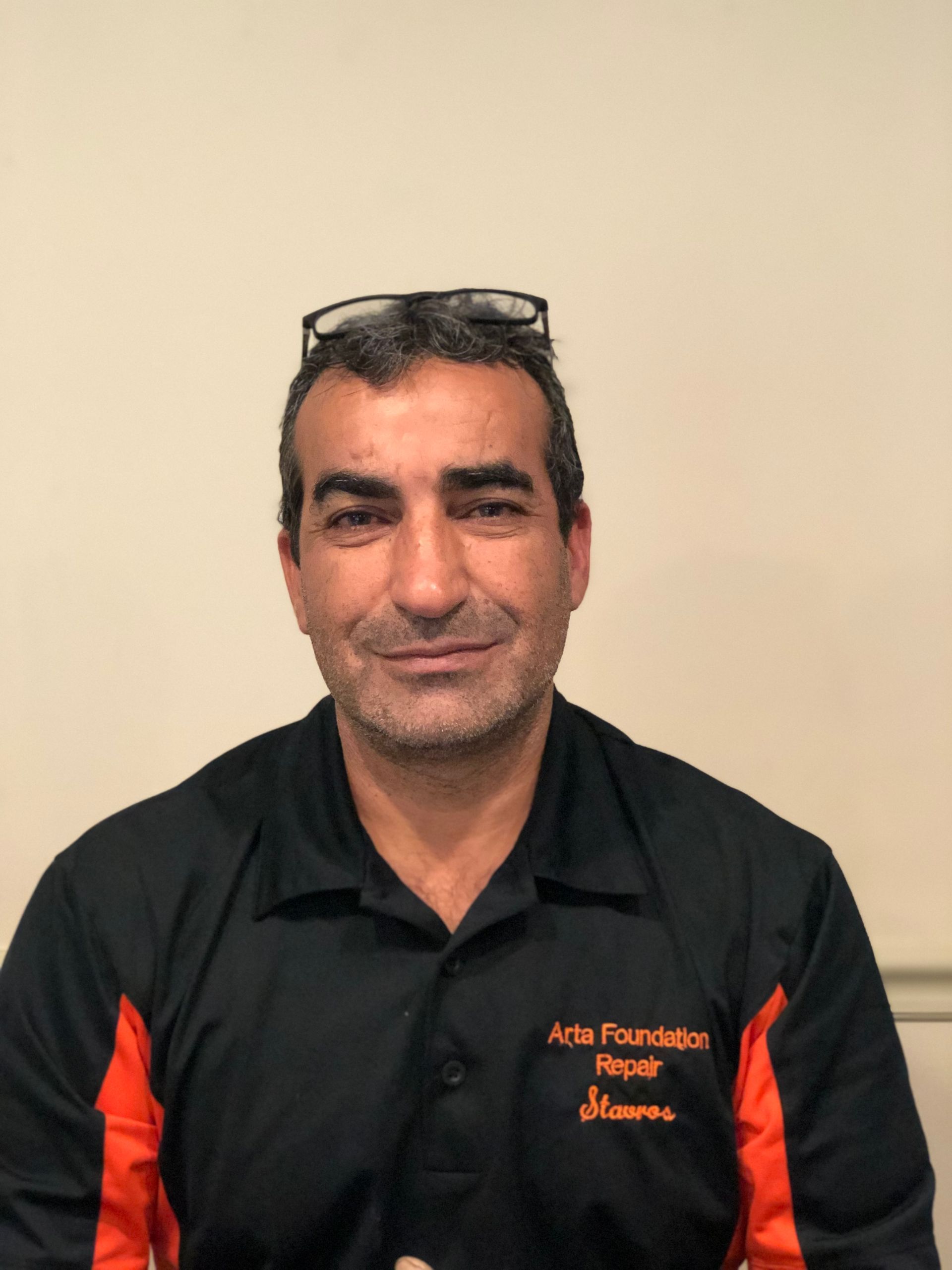 A man with glasses on his head, wearing a black and orange uniform shirt labeled 
