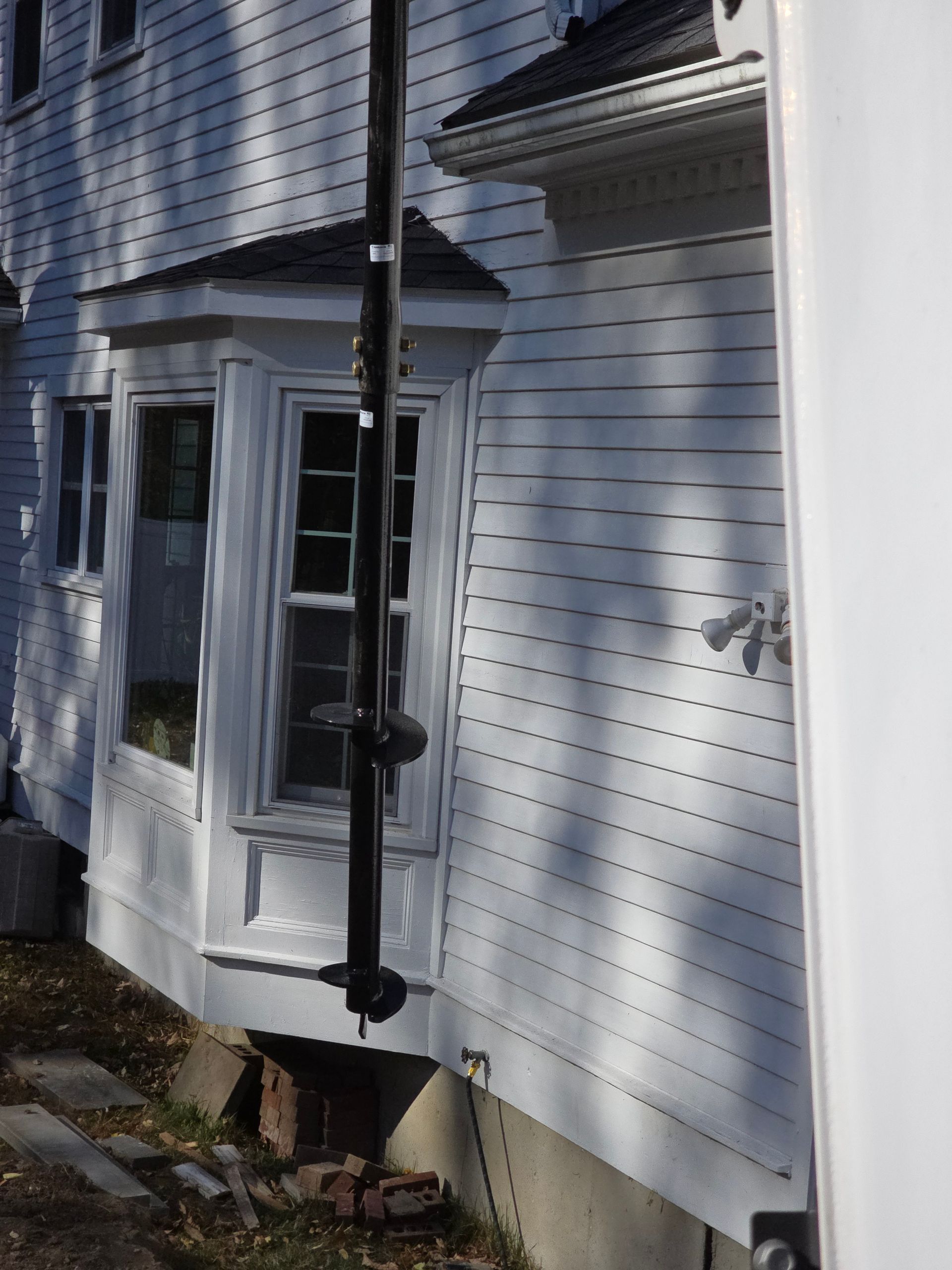 A close-up view of a black telescopic pole positioned vertically against the white exterior of a house with a bay window.