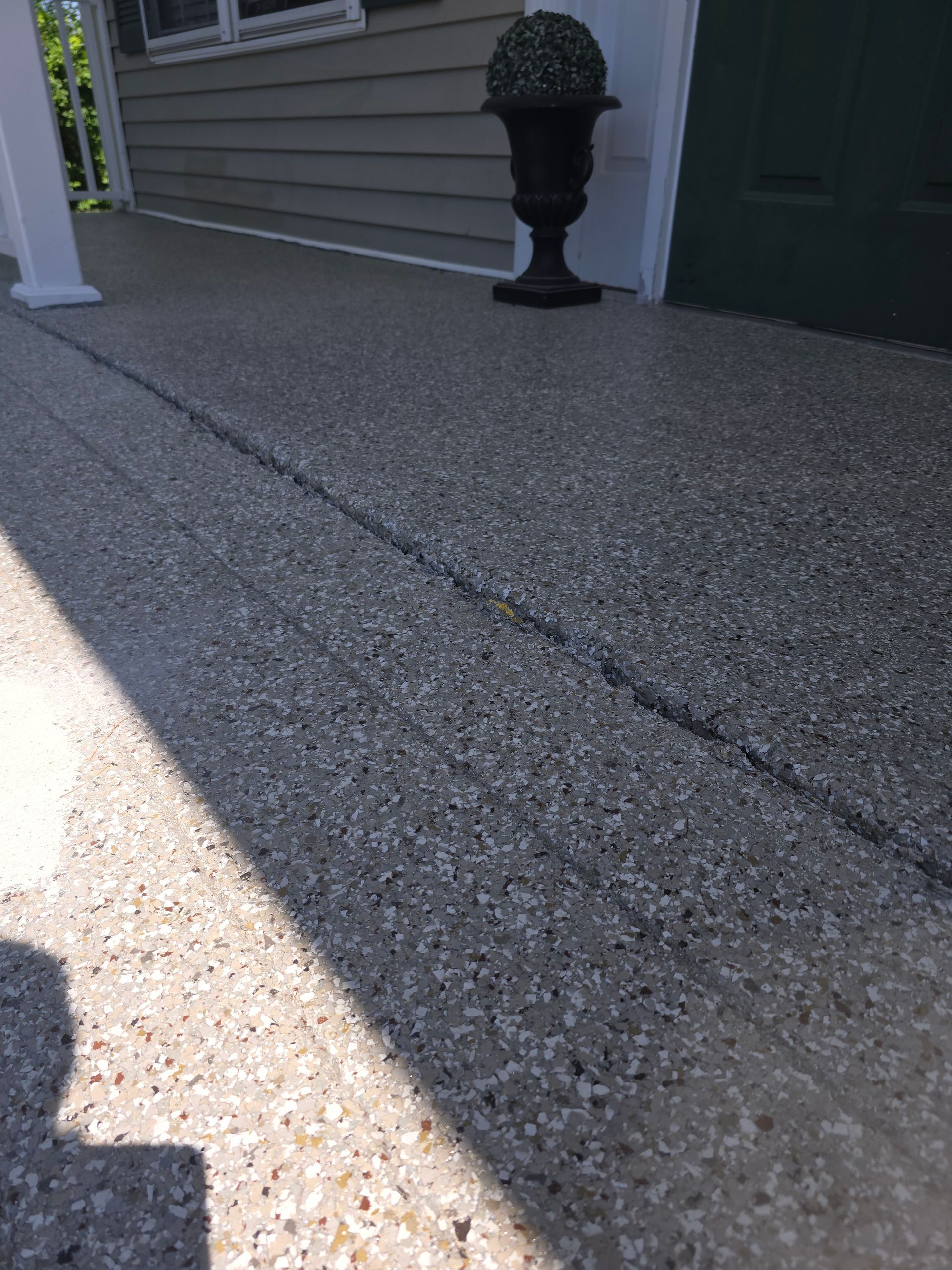 A gray speckled concrete porch floor with a black decorative urn placed near a green door.
