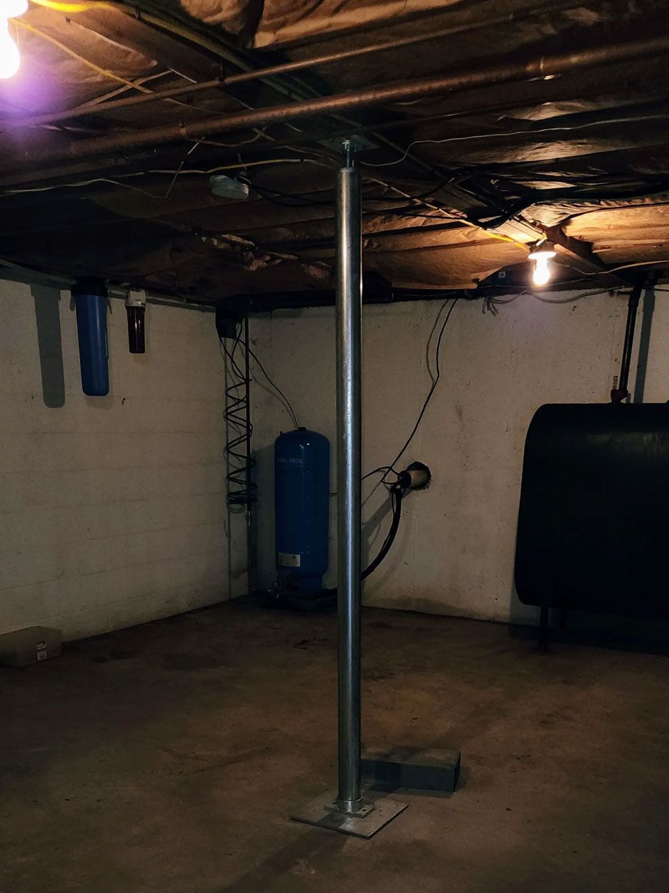 Basement with a central support pole, exposed pipes, and a blue water heater against the wall.