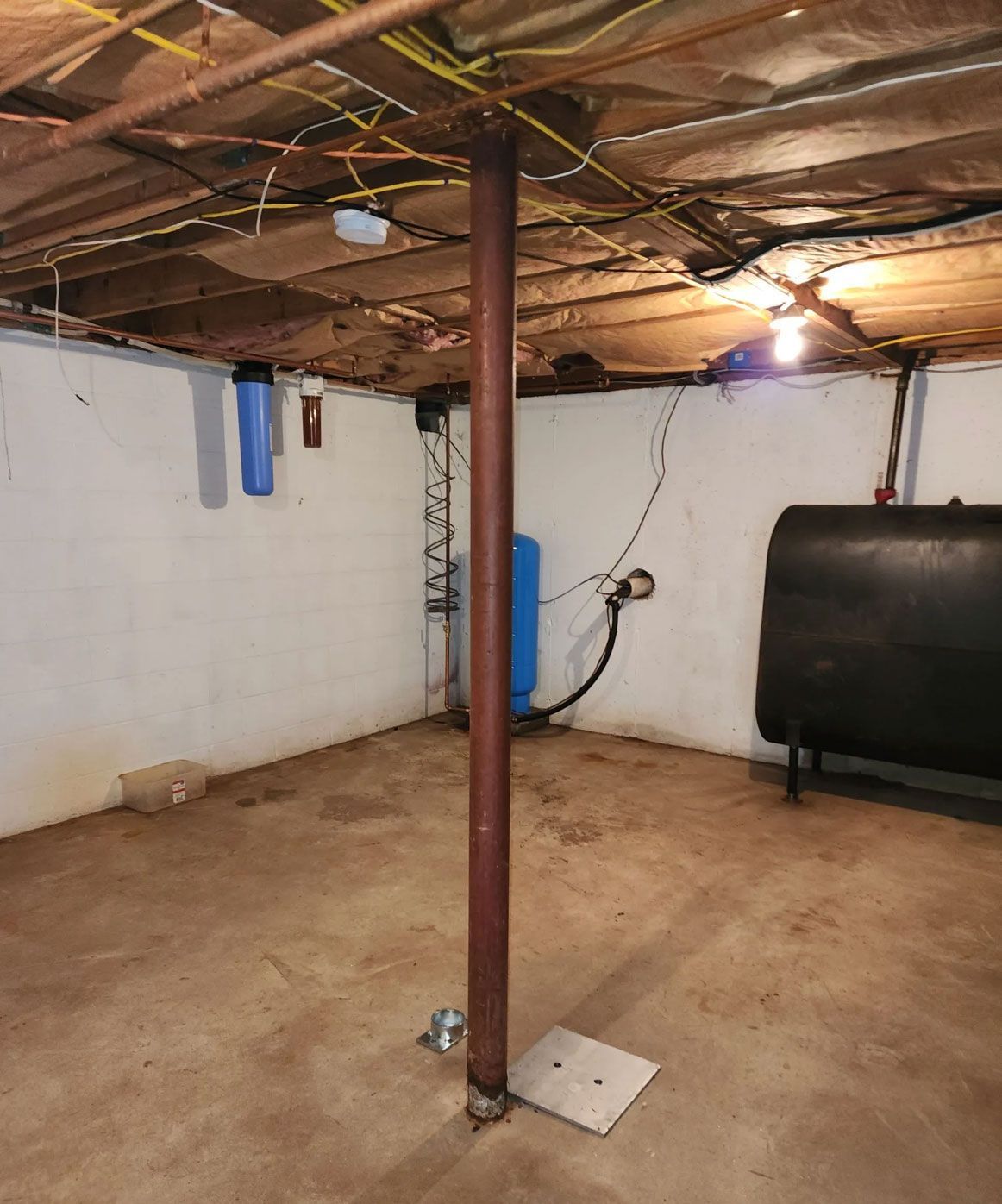 Basement with a central support pole, exposed pipes, and a blue water heater against the wall.