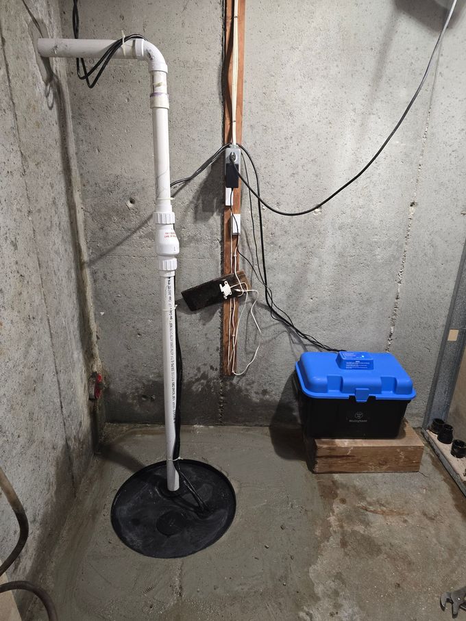 Basement corner with white pipe, exposed wiring, and a blue tool box on a block against a concrete wall.