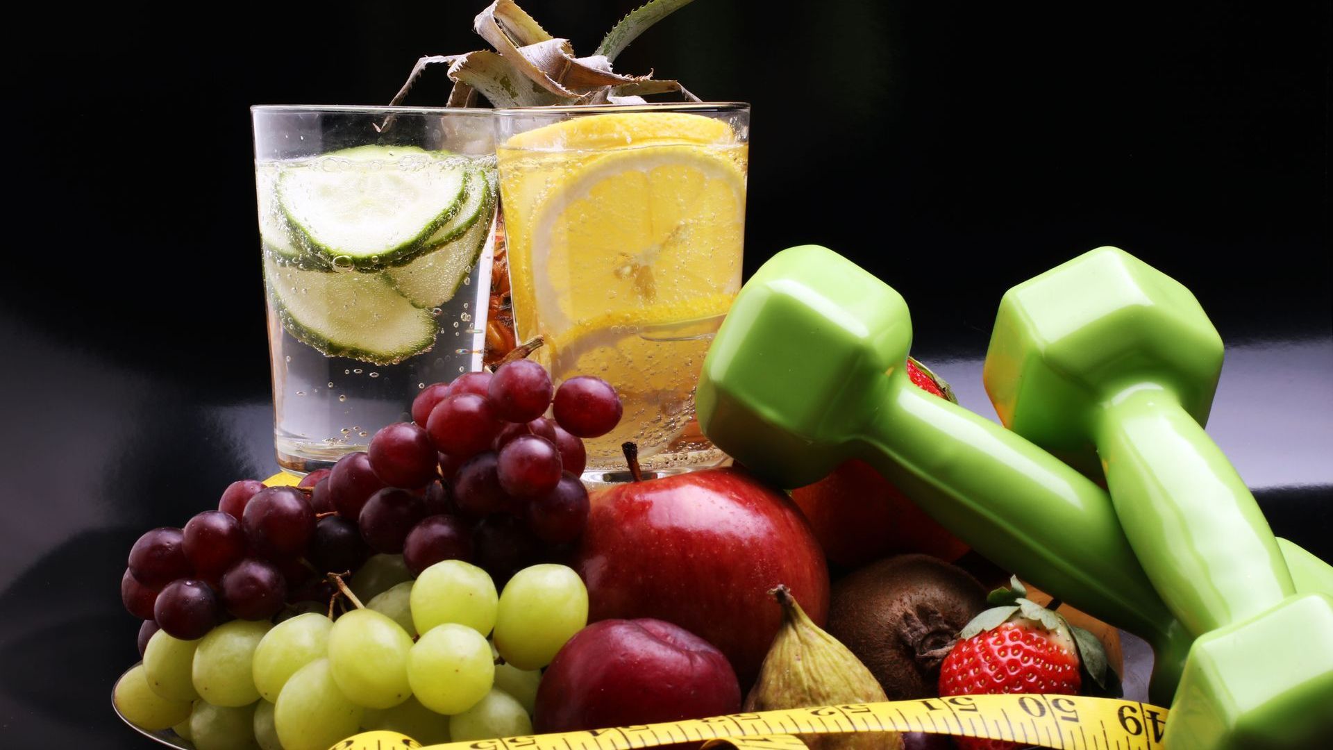 A plate of fruit , dumbbells , a glass of water and a measuring tape.