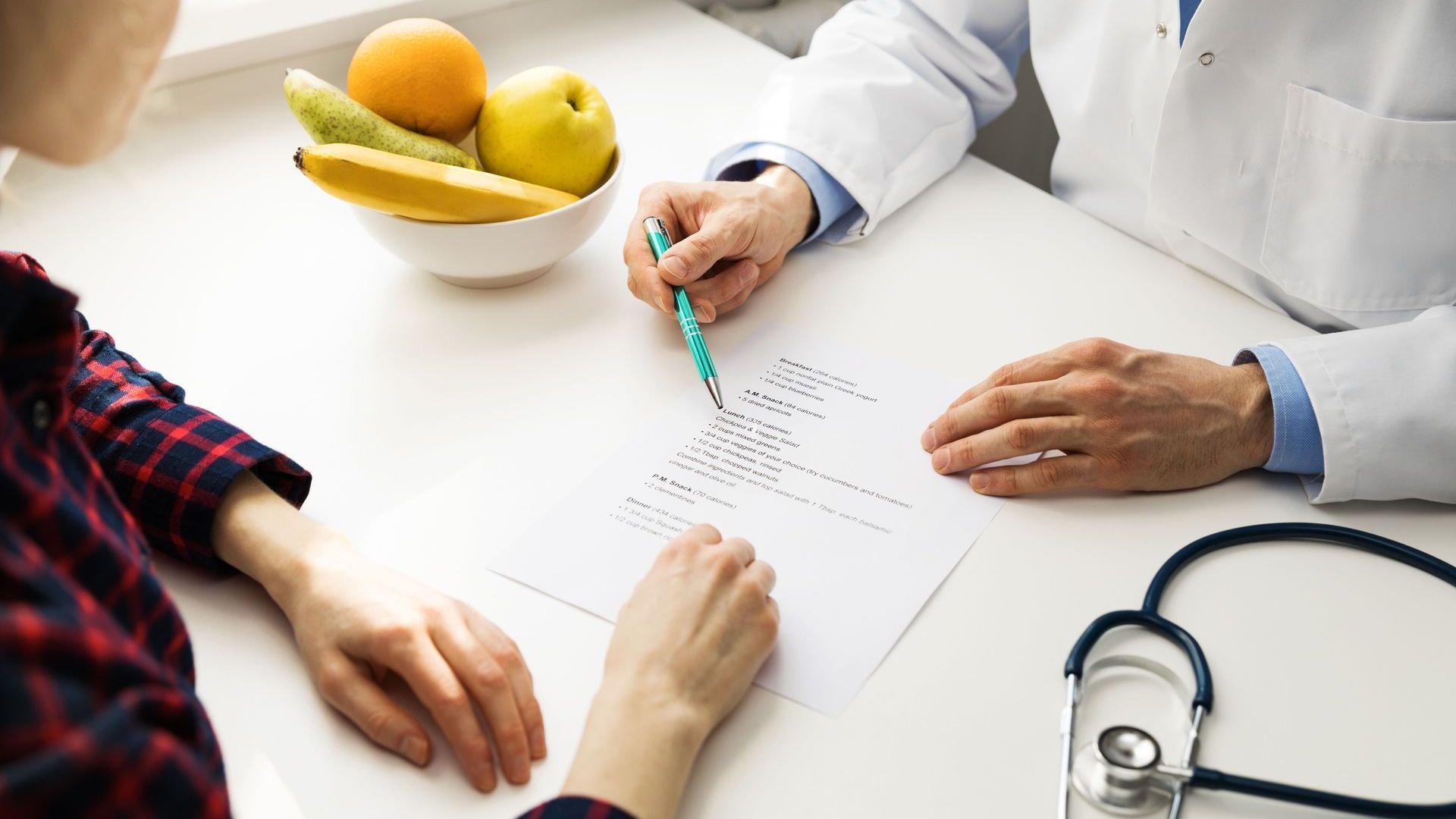 A doctor is talking to a patient who is sitting at a table with a bowl of fruit.