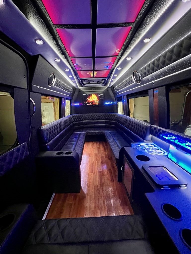 The inside of a shuttle bus with a long couch and a television on the ceiling.