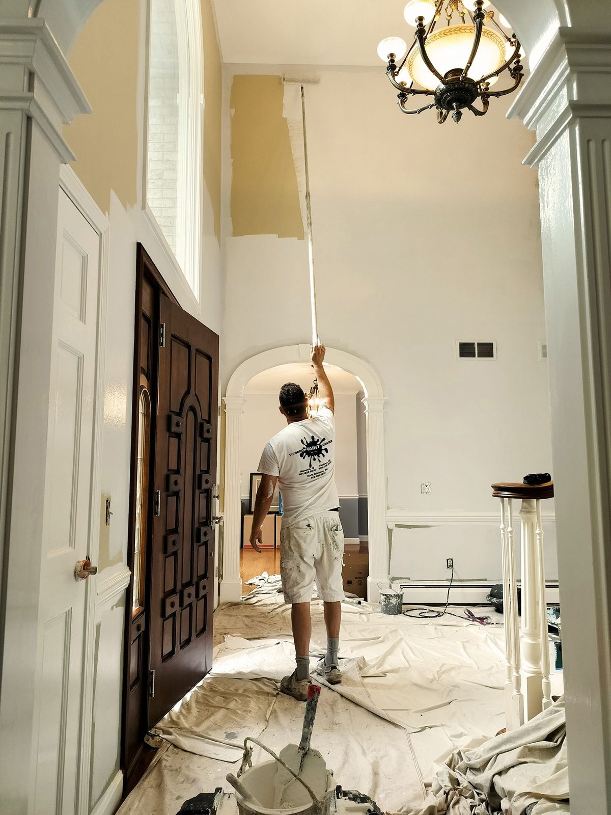 A man is painting a wall with a roller in a hallway.