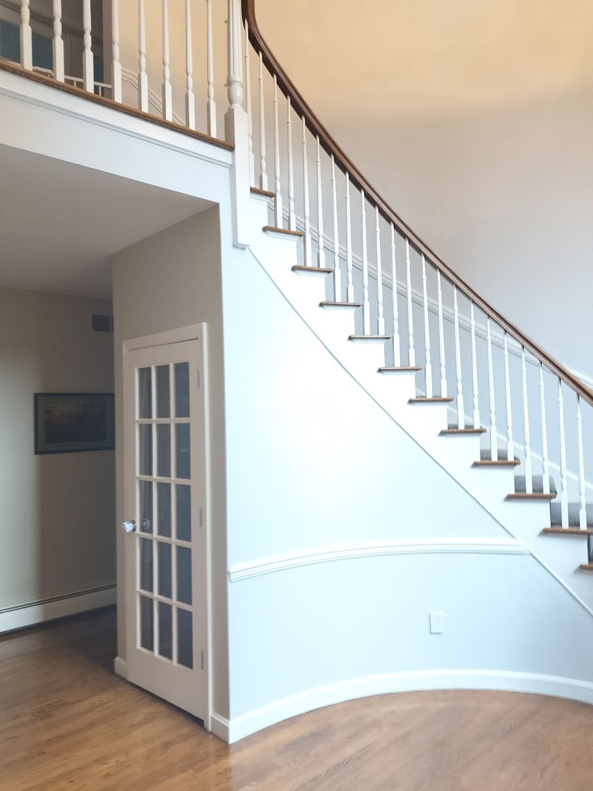 A curved staircase with white railings and a french door