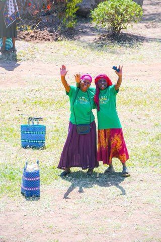 Two children in green shirts and colorful skirts, arms raised, standing outdoors beside two stacked baskets.