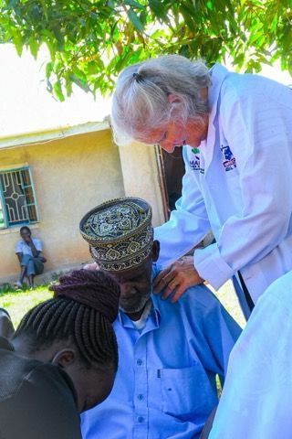 Doctor examining seated man outdoors under a tree.