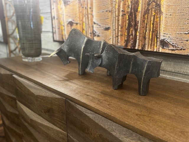 Sculpture of two bulls on a wooden cabinet, with a tall vase and painting in the background.