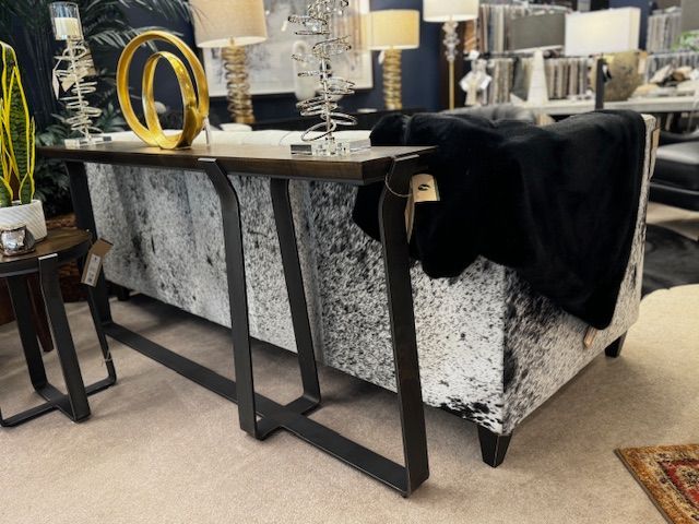 A console table with a black metal frame and a white and black cowhide upholstered sofa in a store.