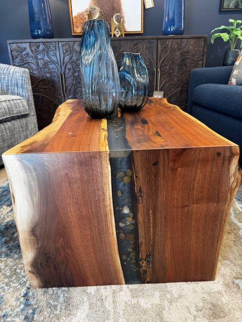 Live edge wooden coffee table with blue vases, near a dark blue couch.