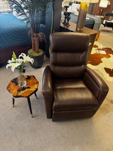 Brown leather recliner next to a patterned side table and a vase of white lilies.