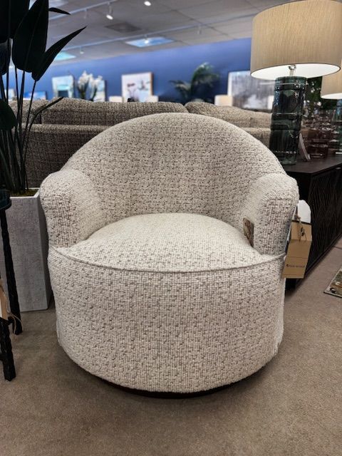 Cream-colored, patterned swivel armchair in a showroom setting.