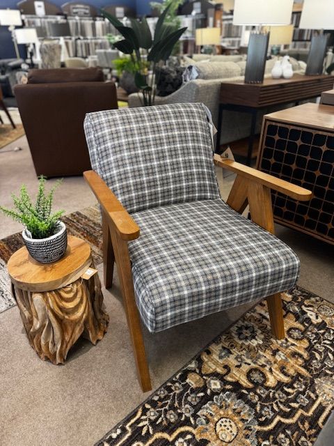 Plaid armchair with wooden frame, next to a wooden stump table with a plant and a patterned rug.