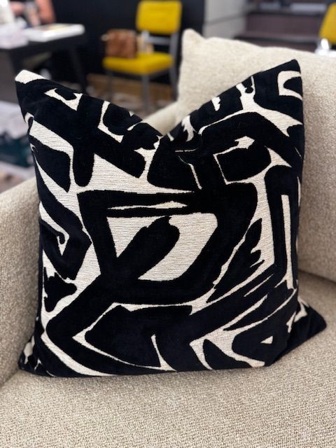 Black and white patterned pillow on a beige couch in a room with a yellow chair.