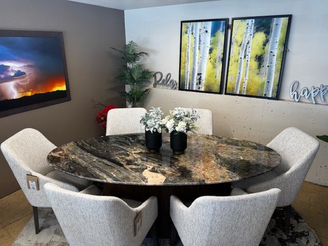 Oval dining table with six white chairs, artwork on the wall, and flower centerpieces.