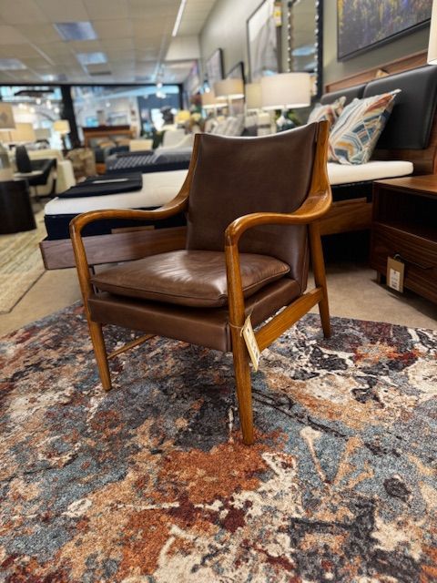 Brown leather armchair with wooden frame on patterned rug in a furniture store.
