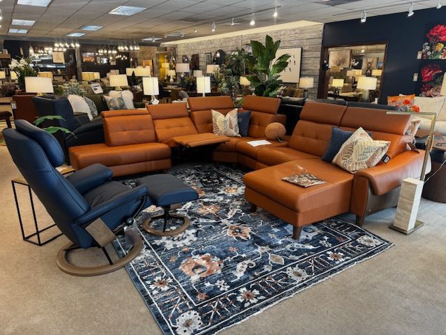 A furniture store displays an orange sectional sofa and a blue recliner chair on a floral rug.