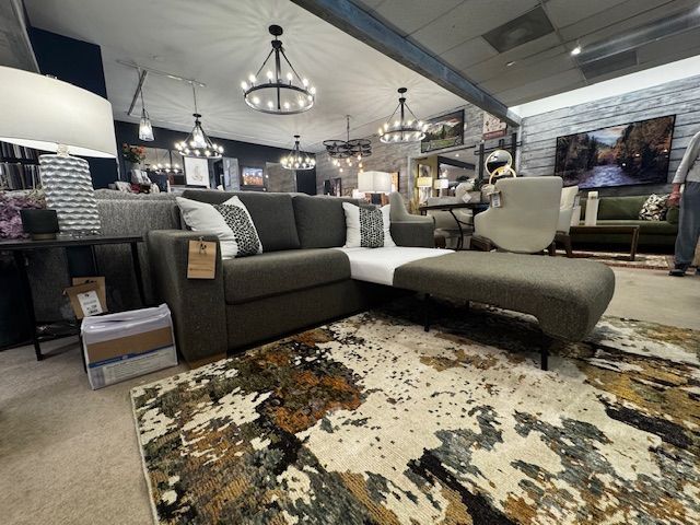 A furniture store displays a dark gray sectional sofa with a chaise lounge on a patterned rug.