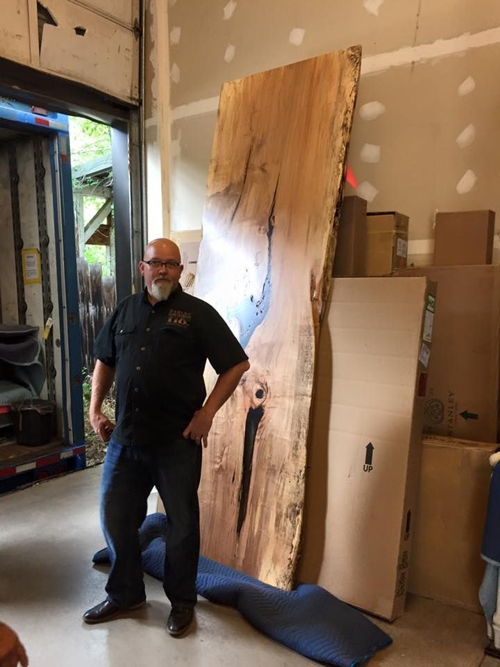 Man standing next to a large, live-edge wooden slab in a workshop setting.