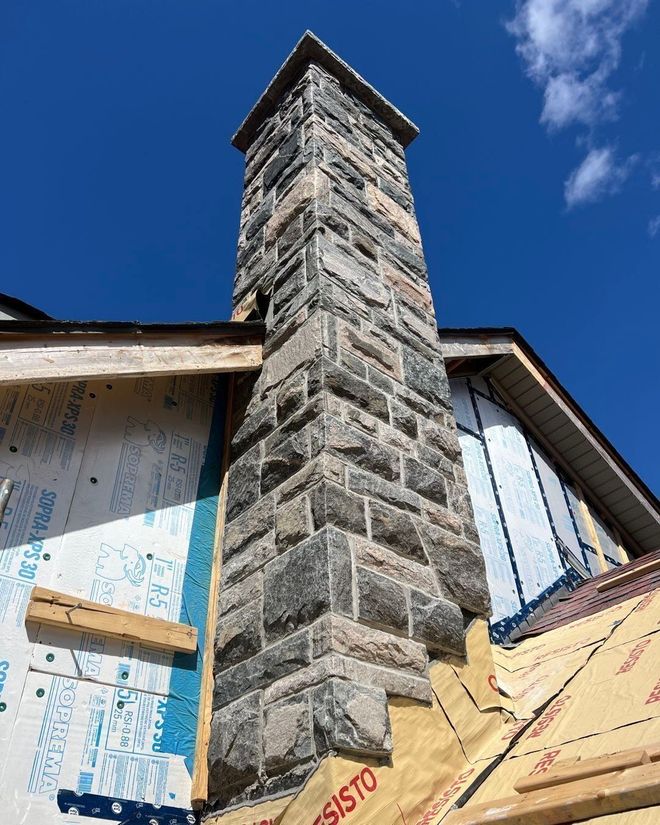 Stone chimney extending from a house under construction; blue sky.
