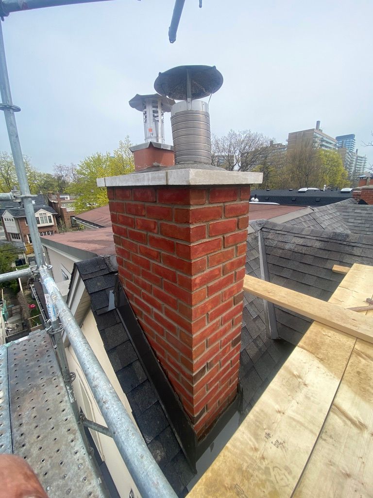 Brick chimney on a rooftop with scaffolding, topped with a metal cap.