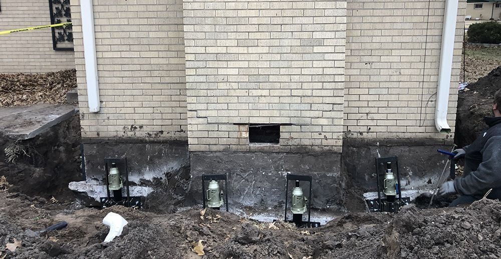 Foundation repair work on a brick building; helical piers installed in the soil along the wall.