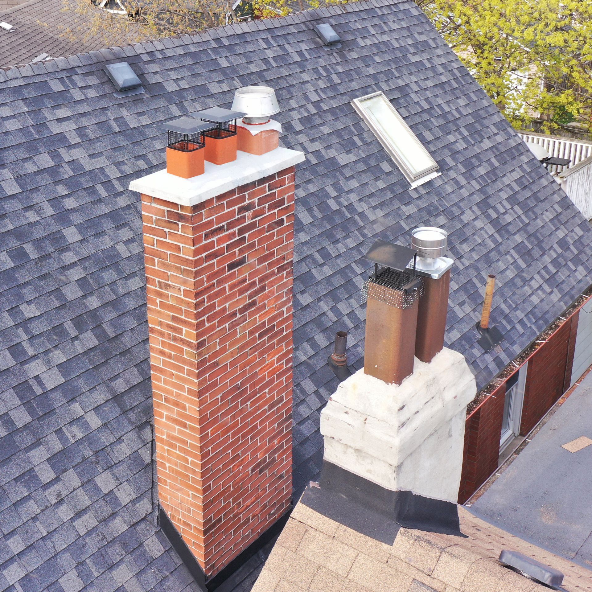 Brick chimneys on a shingled roof with a skylight.