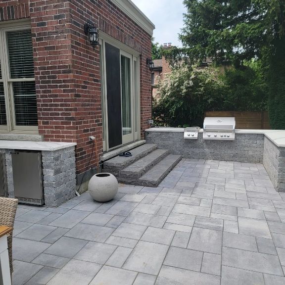 Brick building with gray stone patio, steps, grill, and built-in cooler.