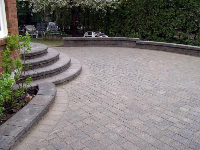 Stone patio with curved steps, low wall, and shrubbery.