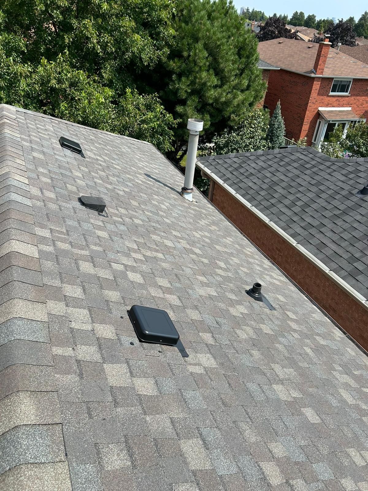 Angled view of a residential roof with asphalt shingles; vents and a chimney are visible.