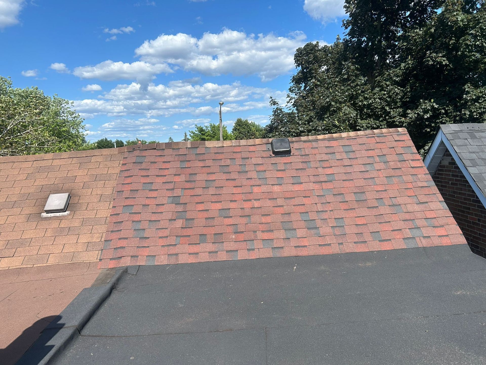 Partially shingled roof with mixed red and brown shingles. Flat, black roof section in foreground.