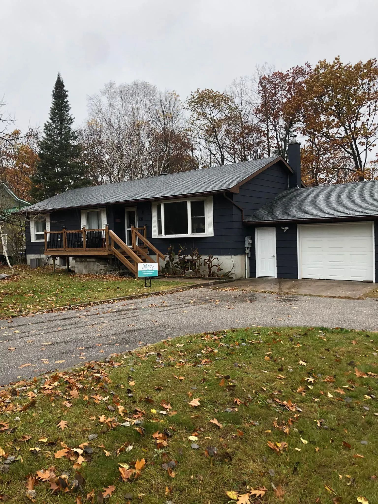 Dark blue house with a gray roof, small porch, and attached garage on a fall day.