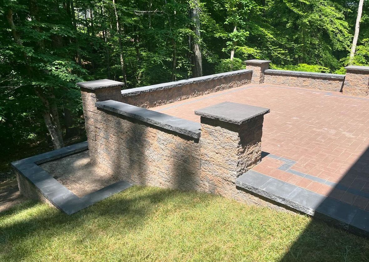 Stone patio with retaining walls, surrounded by grass and trees.