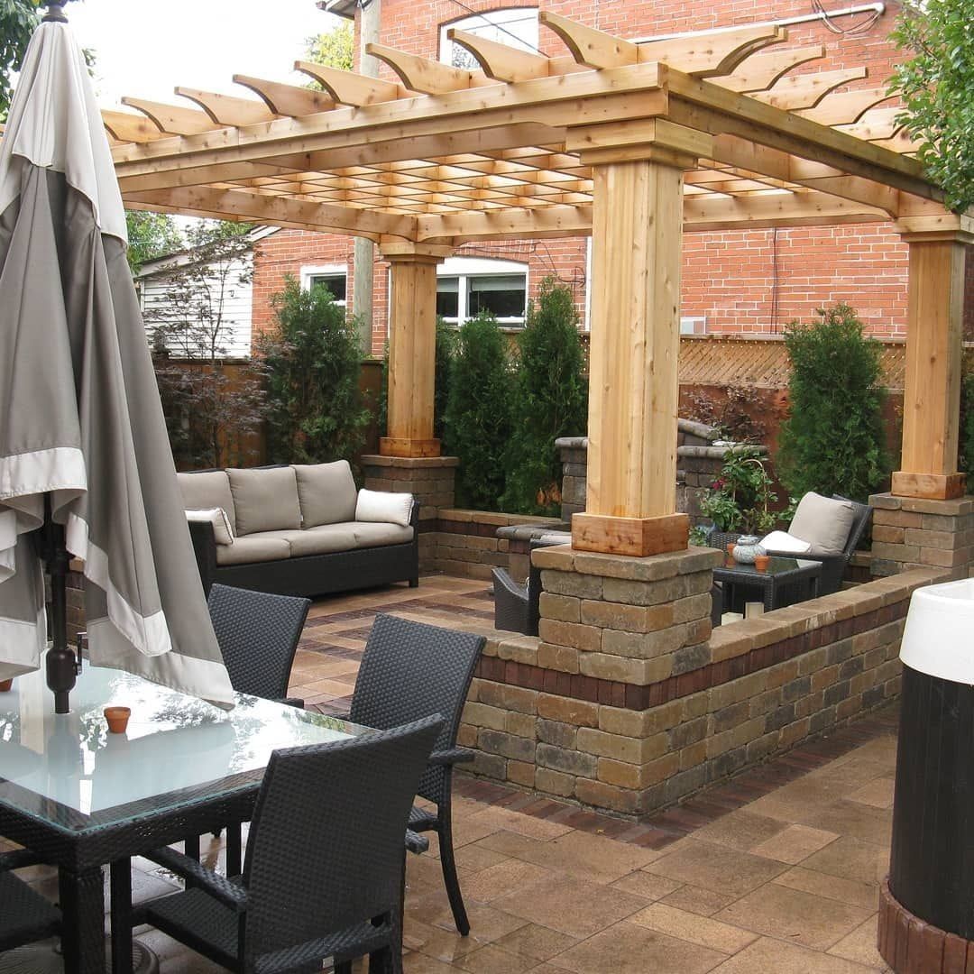 Patio with a pergola, seating area, and dining table, surrounded by brick walls and greenery.