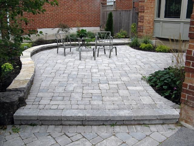 Brick patio with curved retaining wall and seating area, surrounded by brick building and greenery.