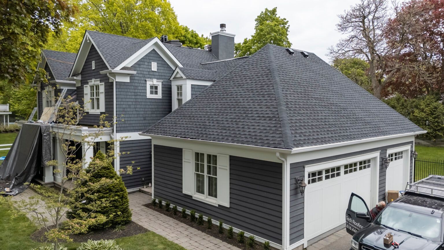 Dark blue house with white trim and a two-car garage. A person is near an open car door.