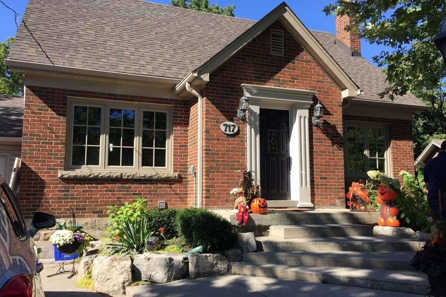 Red brick house with stone steps, front porch decorations, and landscaped garden.