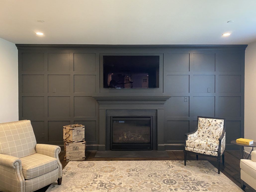 Dark paneled wall with fireplace, TV, and two armchairs in a custom basement.