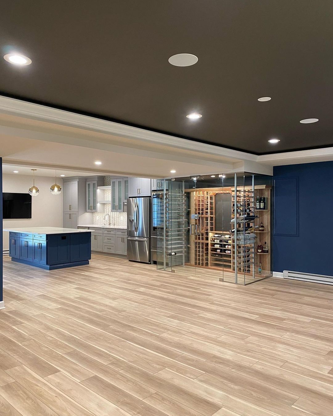 Spacious kitchen with blue island, stainless steel appliances, and glass-enclosed wine cellar. Dark blue and gray tones.