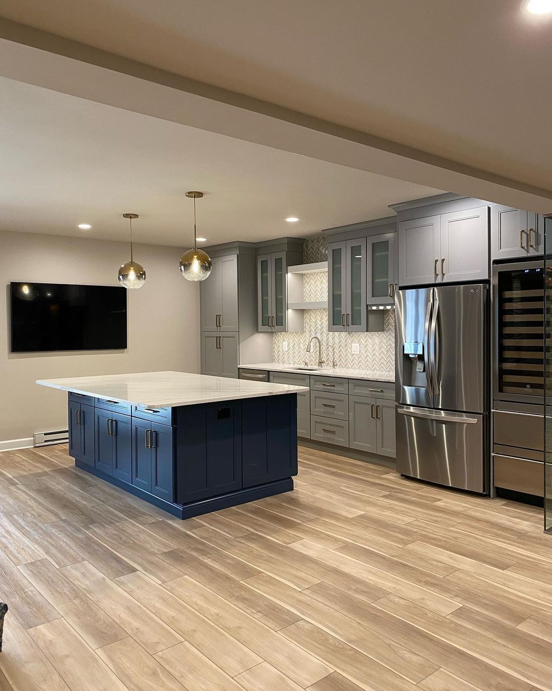 Modern kitchen with blue island and gray cabinets, stainless steel appliances, and wood floors.
