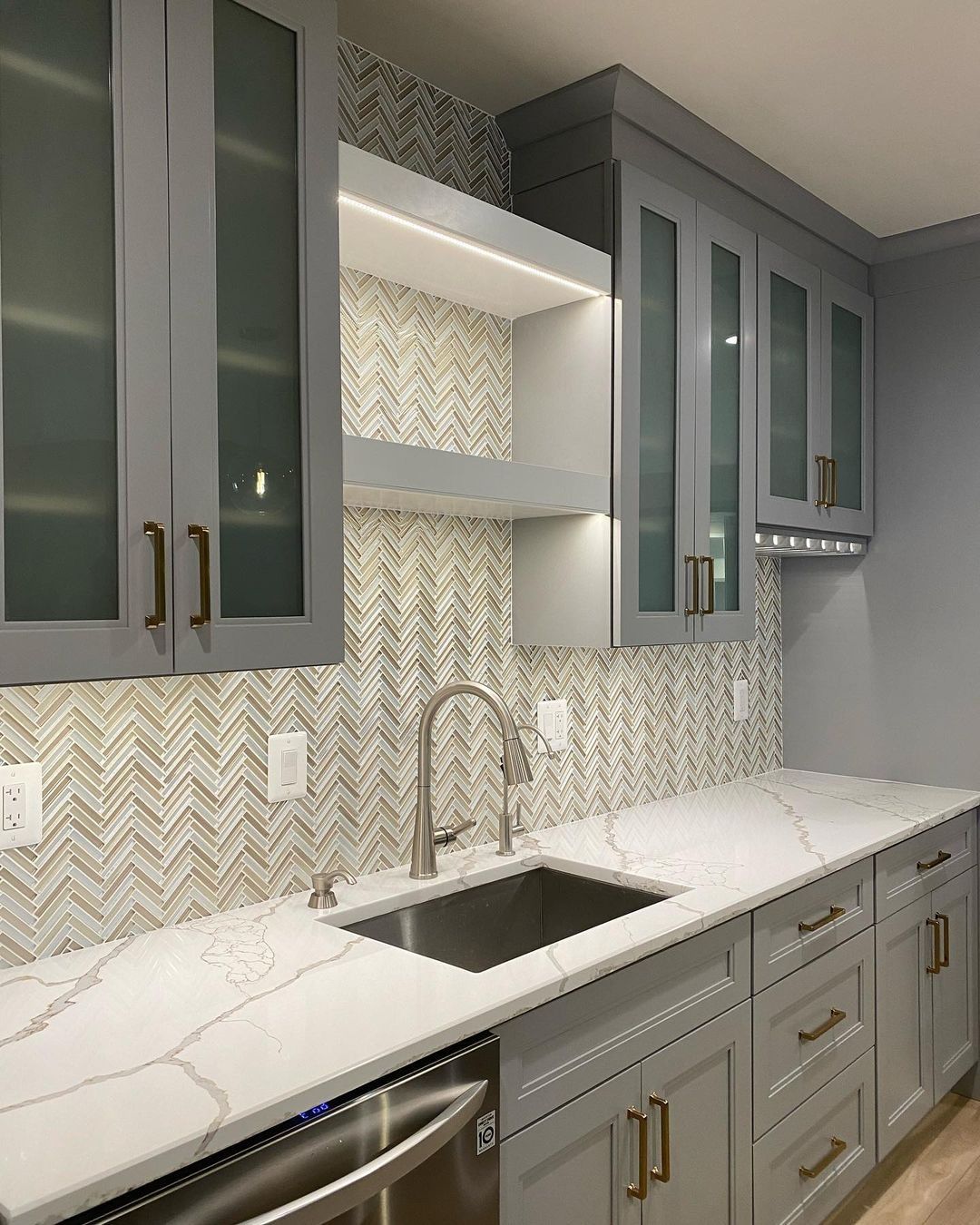 Gray kitchen with white countertops, mosaic backsplash, and stainless steel sink.