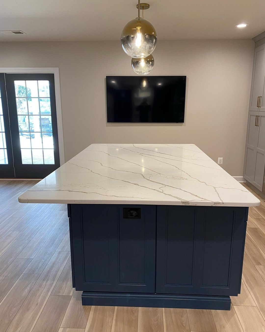 Kitchen island with blue cabinets and white countertop, a TV, and a pendant light fixture.