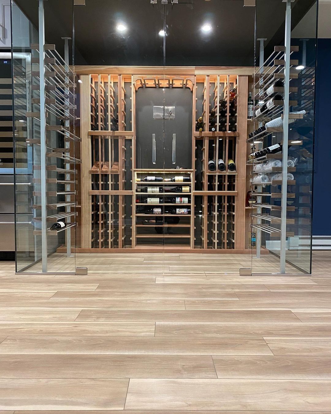 Wine cellar with wooden wine racks and glass doors on light wood floor.