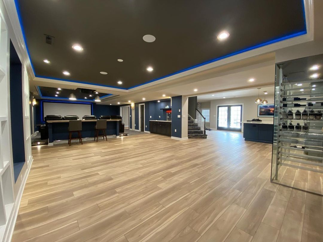 Spacious finished basement with wooden floors, bar area, and wine storage. Dark ceiling with blue trim.