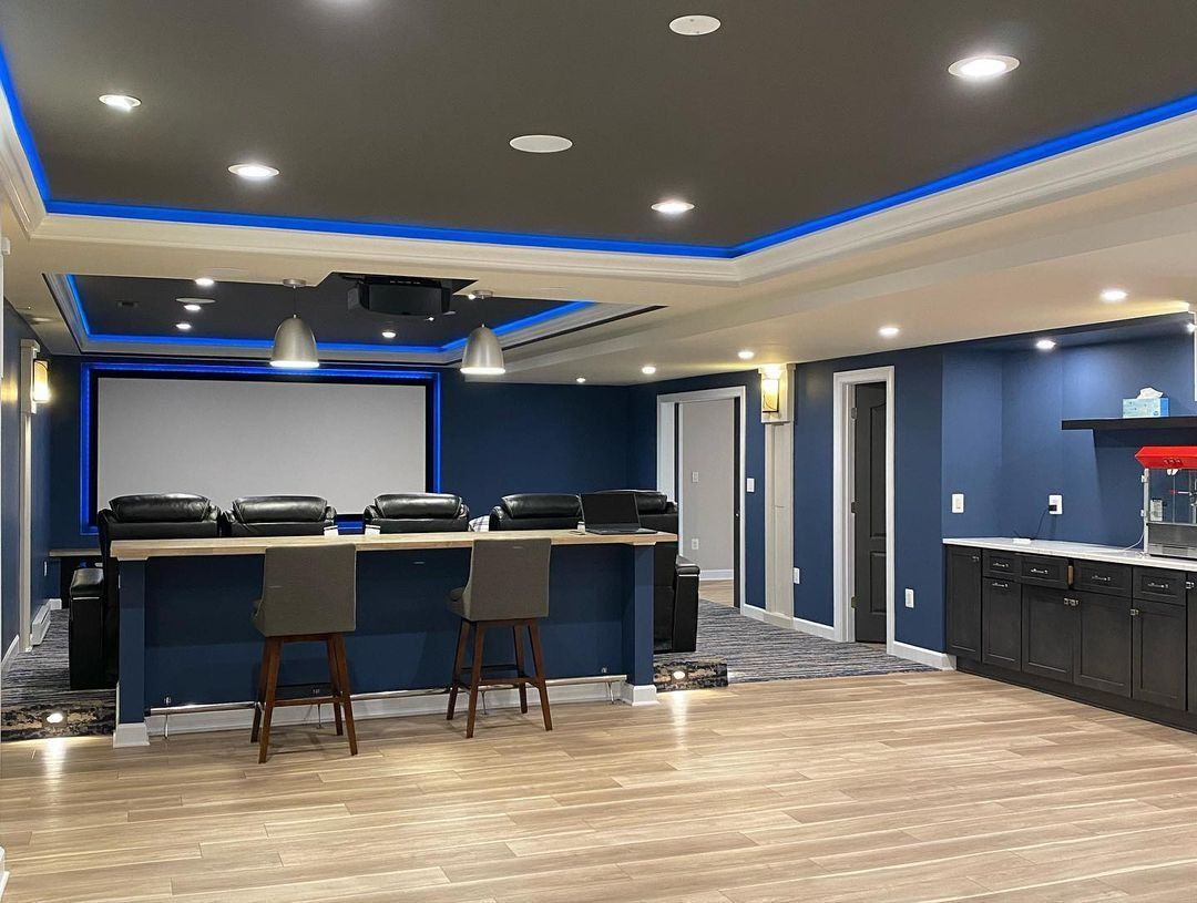 Home theater with screen, projector, blue accent lights, bar seating, popcorn machine, and blue walls.